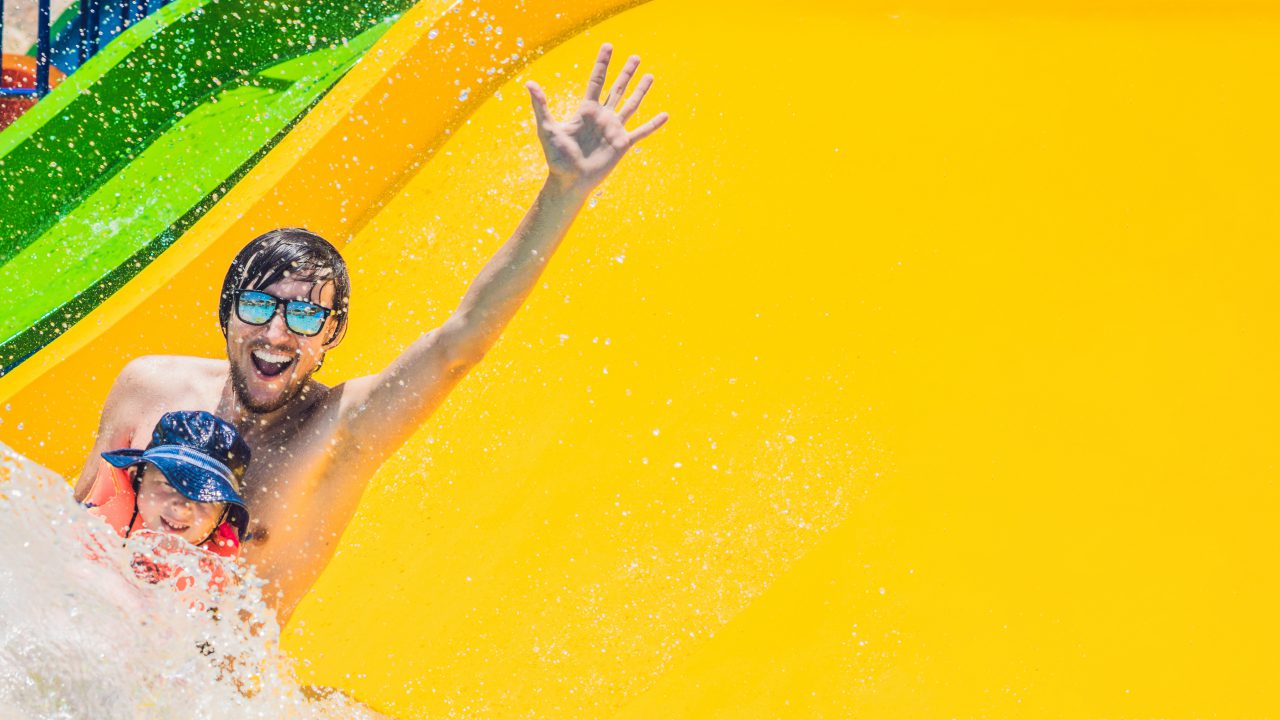 Parchi a tema Toscana - BANNER Father and son on a water slide in the water park. Long Format. Parchi a tema Toscana - BANNER Father and son on a water slide in the water park. Long Format.